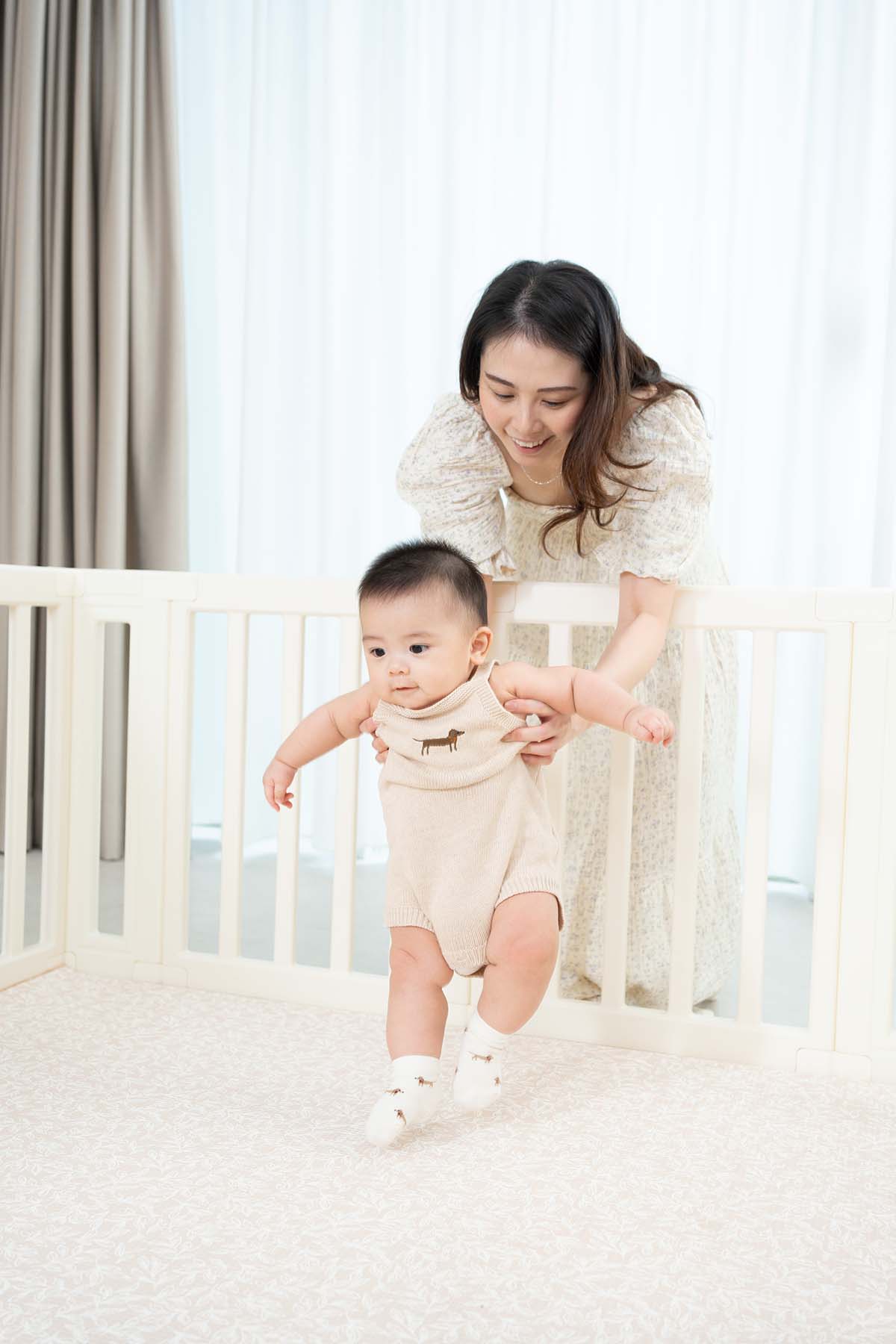 Woman helping a baby stand in a crib